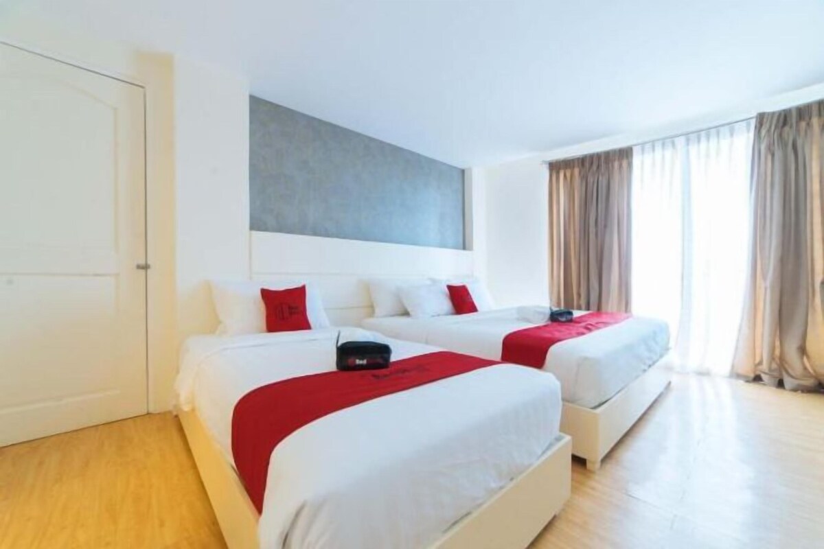 A hotel room with two beds, a large window with curtains, and a white door.