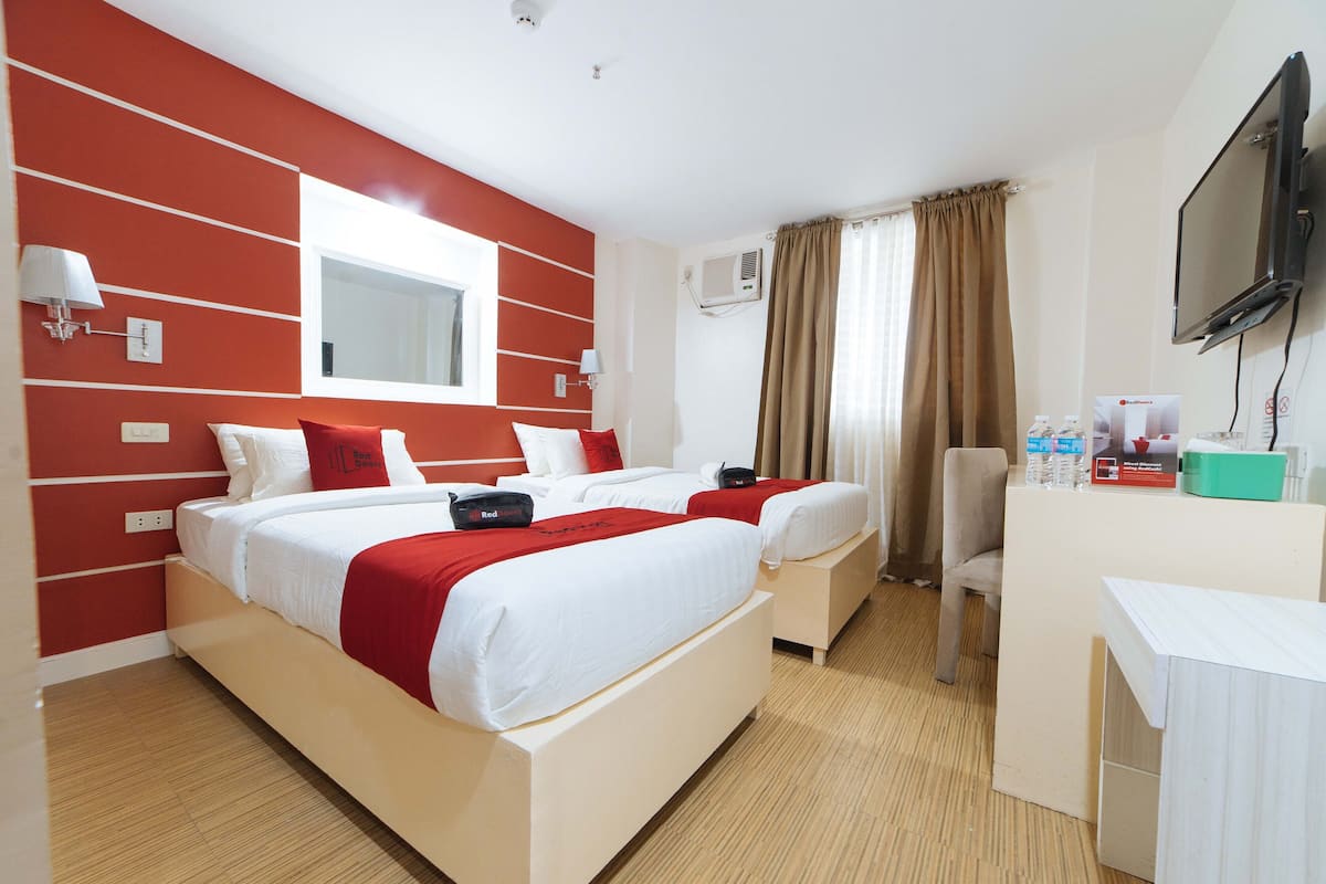 A hotel room with two beds, a desk, a chair, a TV, and a window with curtains.