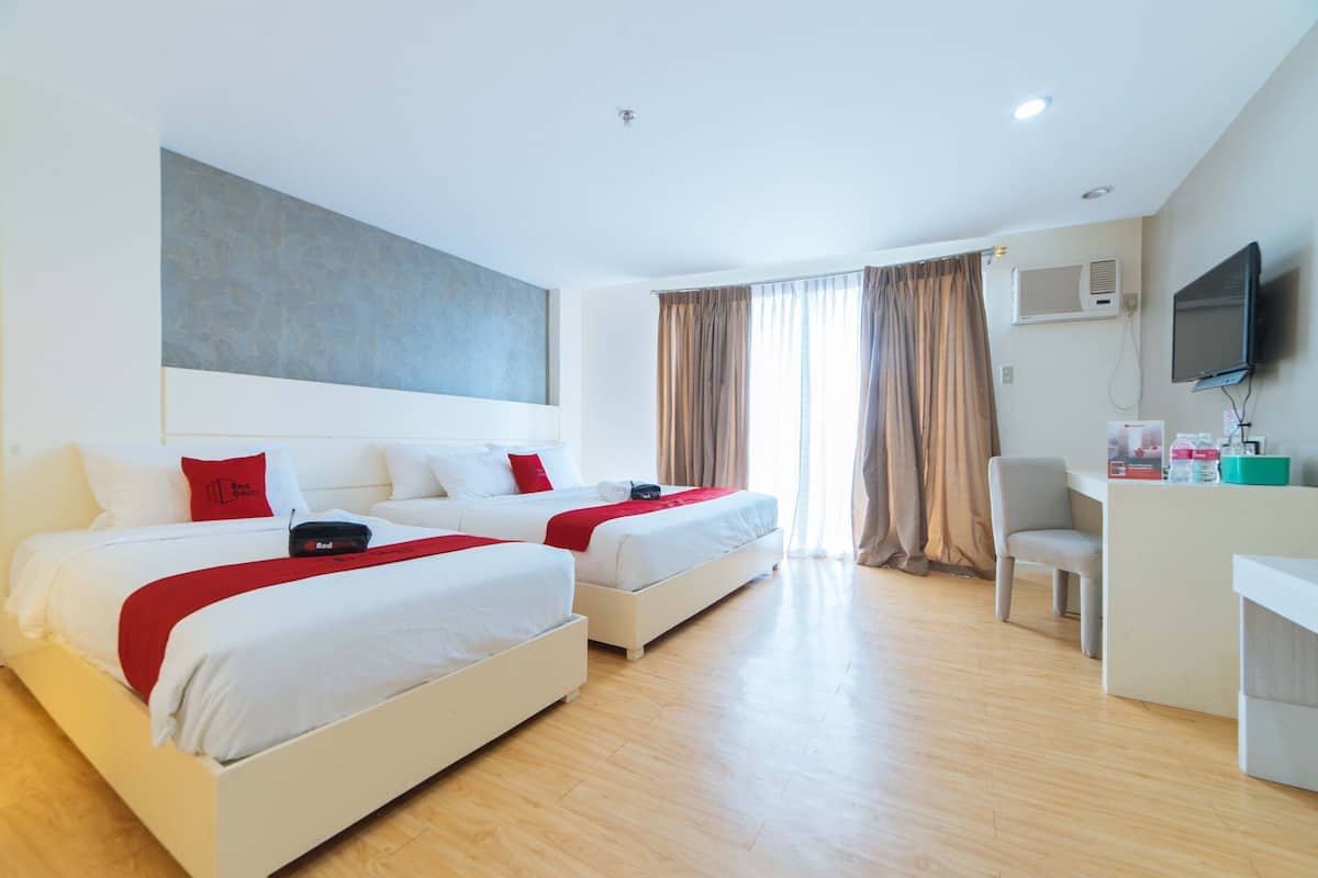 A hotel room with two beds, a desk, a TV, and an air conditioning unit.