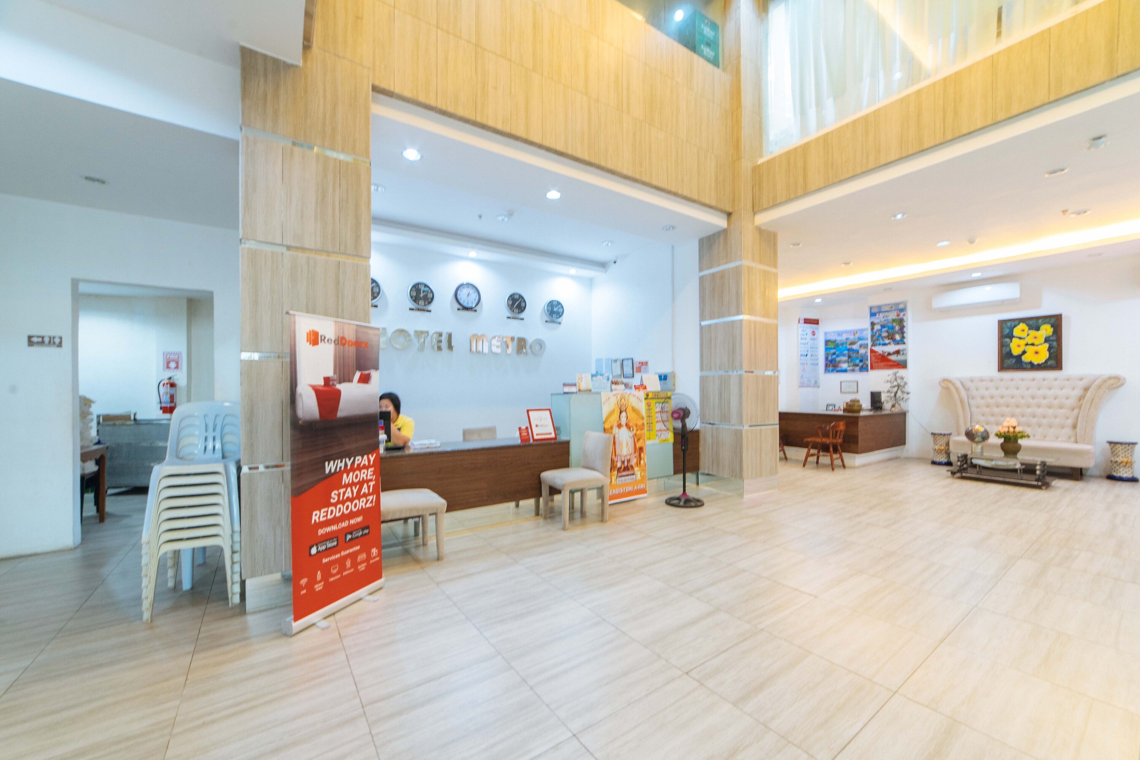 Et hotellets reception område med en træreception, flere stole, en disk med skilt og en væg med ure.