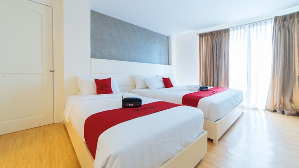 Une chambre d’hôtel avec deux lits, une grande fenêtre avec des rideaux et un tableau abstrait moderne accroché au mur.