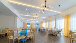 Un vaste espace dédié à la salle à manger, comprenant plusieurs tables et chaises, des luminaires modernes et de grandes fenêtres équipées de rideaux.