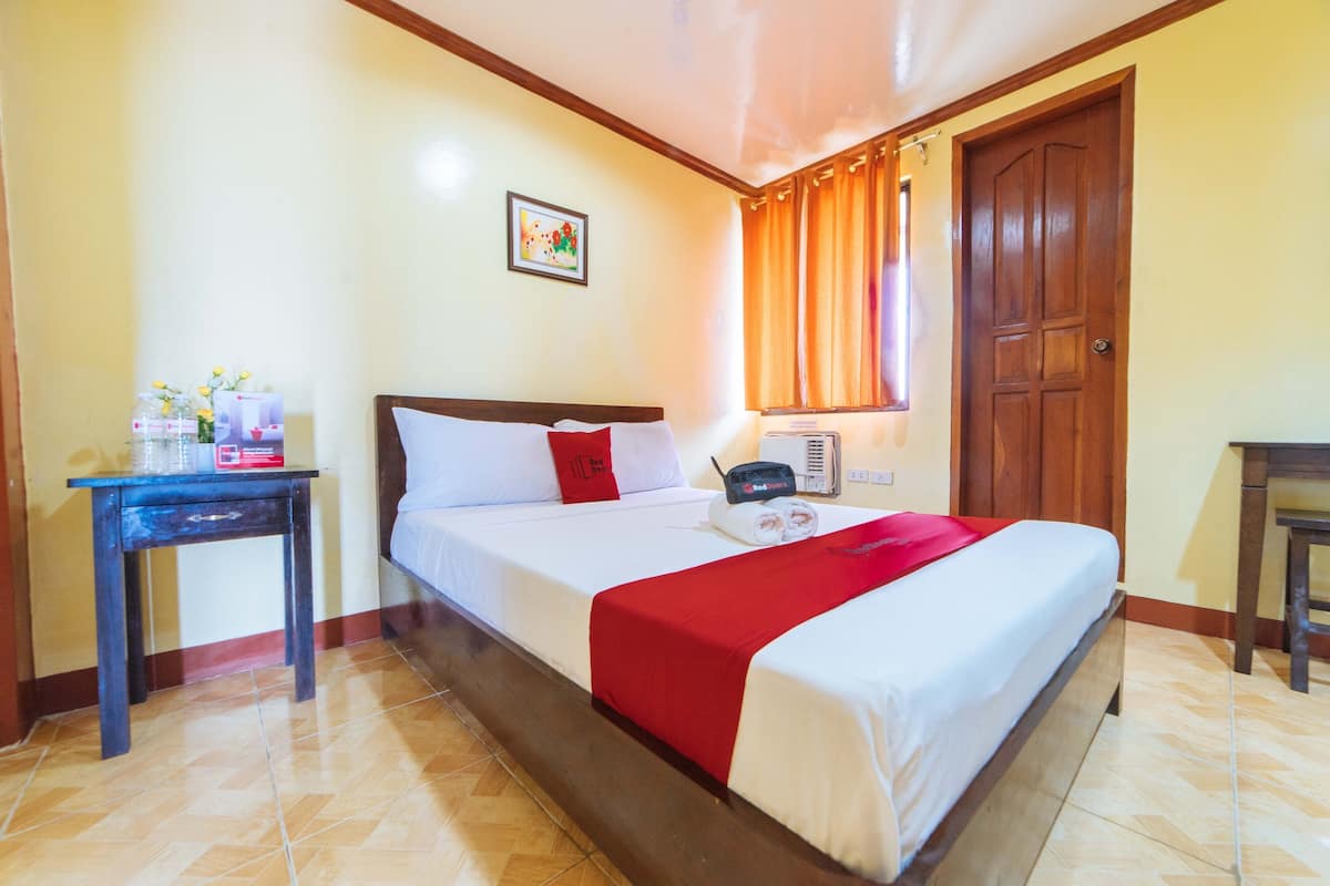 Une chambre d’hôtel comprenant un lit, une table de chevet, un bureau, une fenêtre avec des rideaux et une porte.
