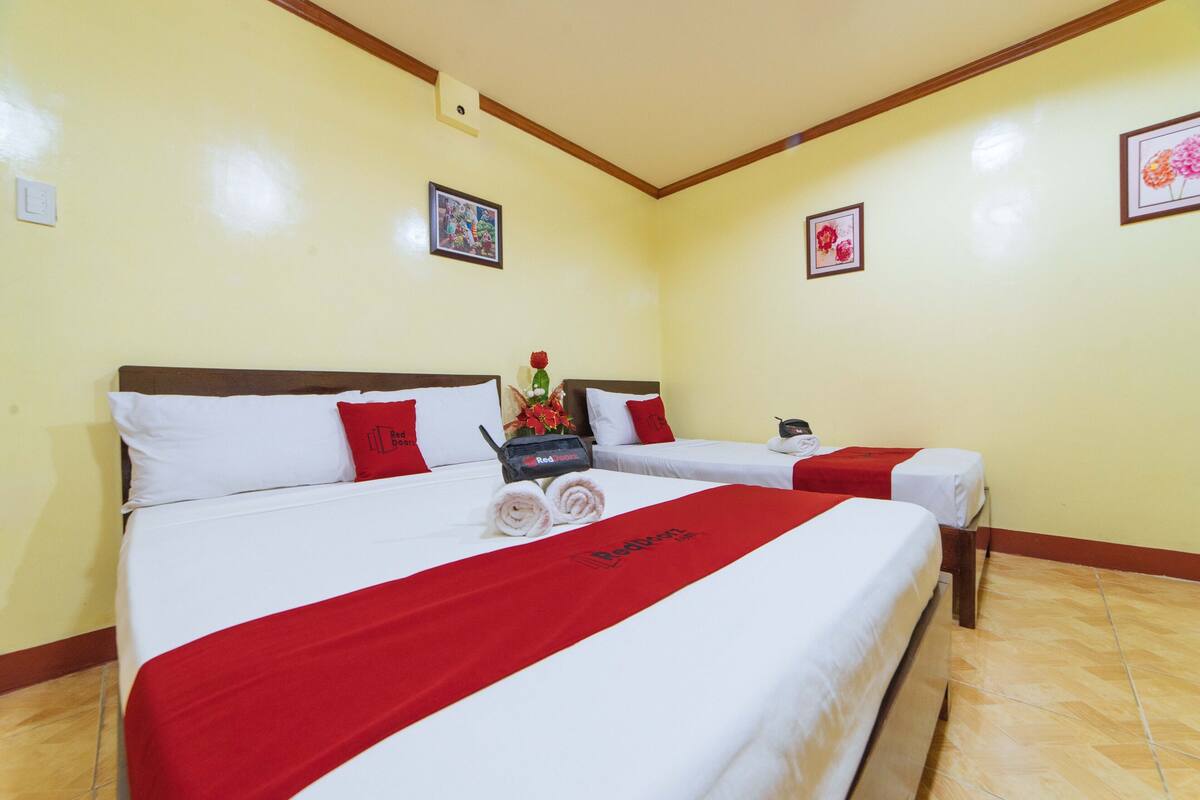 Une chambre d’hôtel avec deux lits, chacun agrémenté de draps blancs et de touches de couleur rouge, d’un plaid rouge et d’une petite table sur laquelle est posé un vase de fleurs.