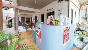 A reception desk with a RedDoorz sign, a quiet please sign, and a check in sign. There are plants around the desk and a staircase in the background. - RedDoorz @ Aparente Gensan (General Santos)