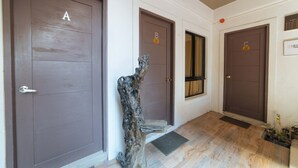 A hallway with three doors labeled A, B, and C, wooden flooring, and a decorative tree trunk. - RedDoorz @ Aparente Gensan (General Santos)