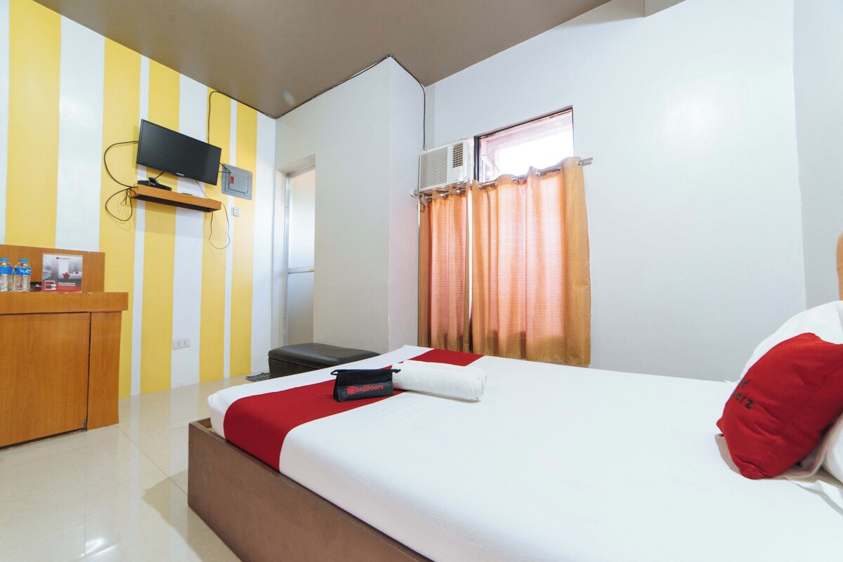Quarto de hotel com cama, secretária, televisão e janela com cortinas.