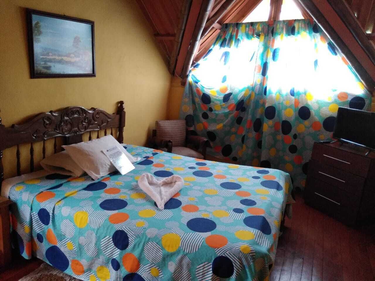 Une chambre à coucher comprenant un lit, une tête de lit en bois, une table de chevet, un téléviseur et une fenêtre avec des rideaux.