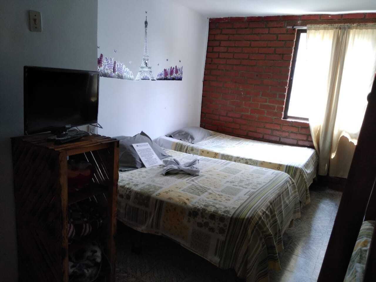 A room with two beds, a television on a wooden stand, and a brick wall.