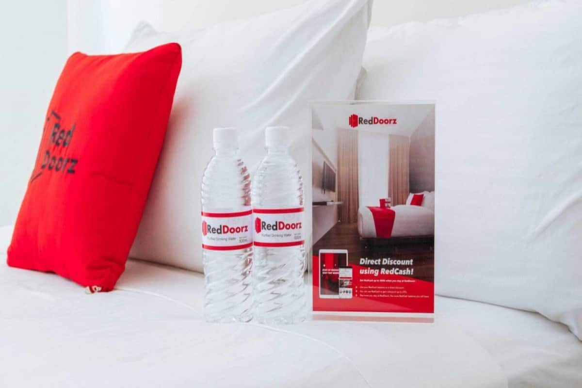 Une chambre d’hôtel avec un lit, deux bouteilles d’eau de la marque RedDoorz et une brochure promotionnelle.