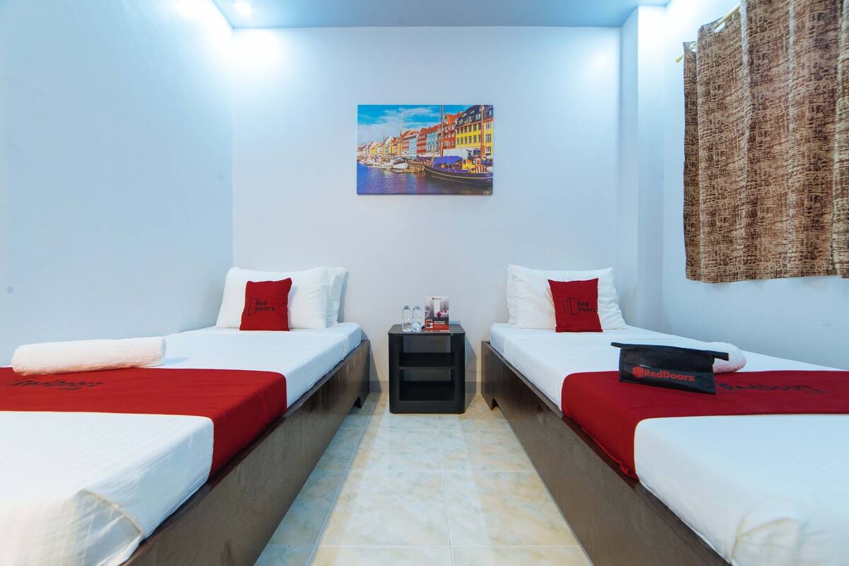 Une chambre d’hôtel avec deux lits, une petite table, un tableau au mur et un rideau.