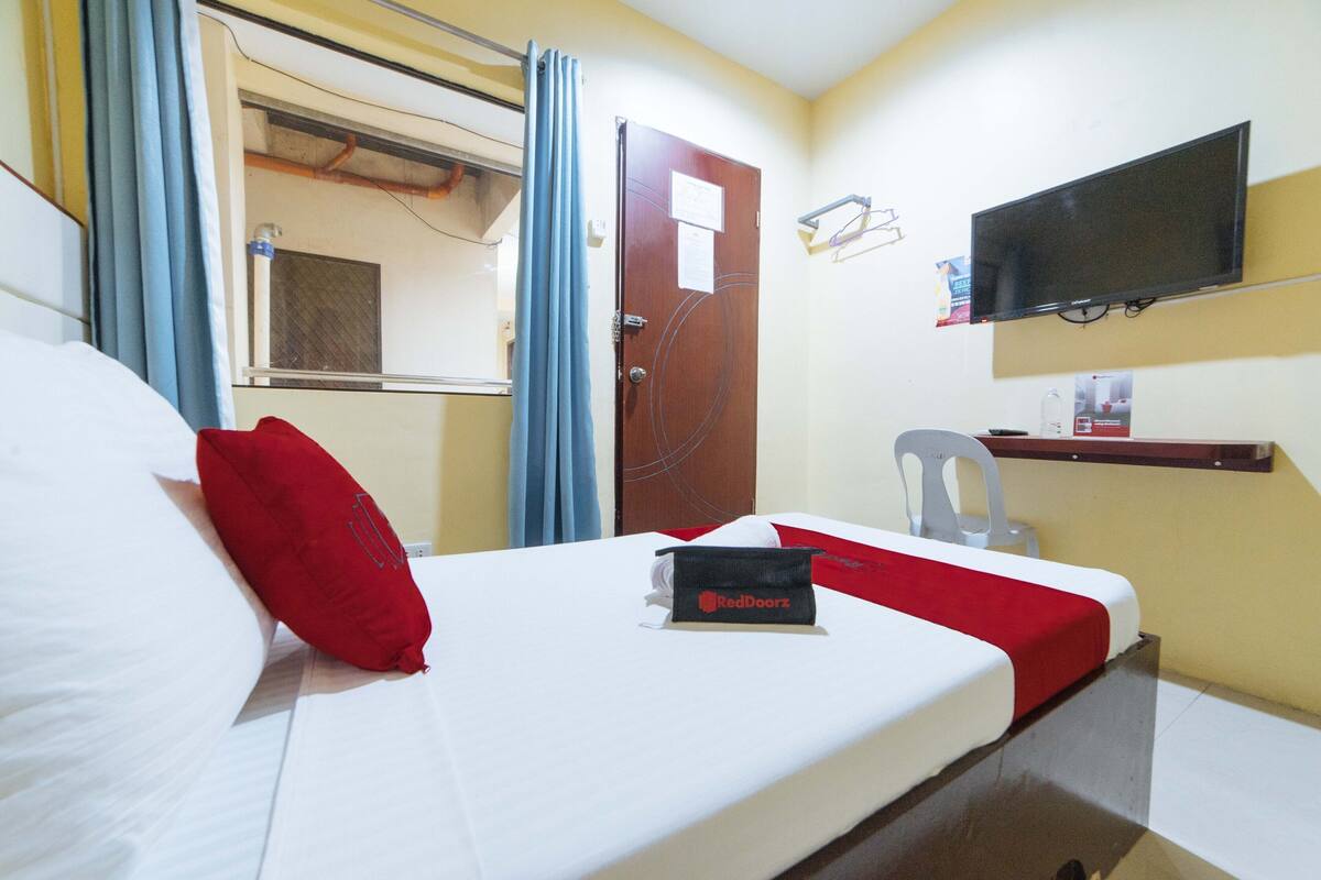 Une chambre d’hôtel équipée d’un lit, d’une télévision, d’une chaise et d’une étagère avec quelques objets.