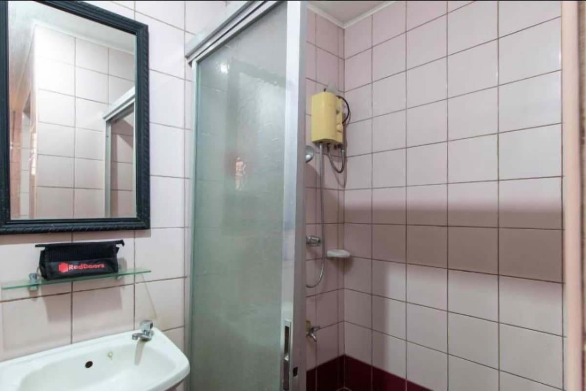 A bathroom with a glass shower enclosure, a white sink, a mirror, and a RedDoor towel rack.