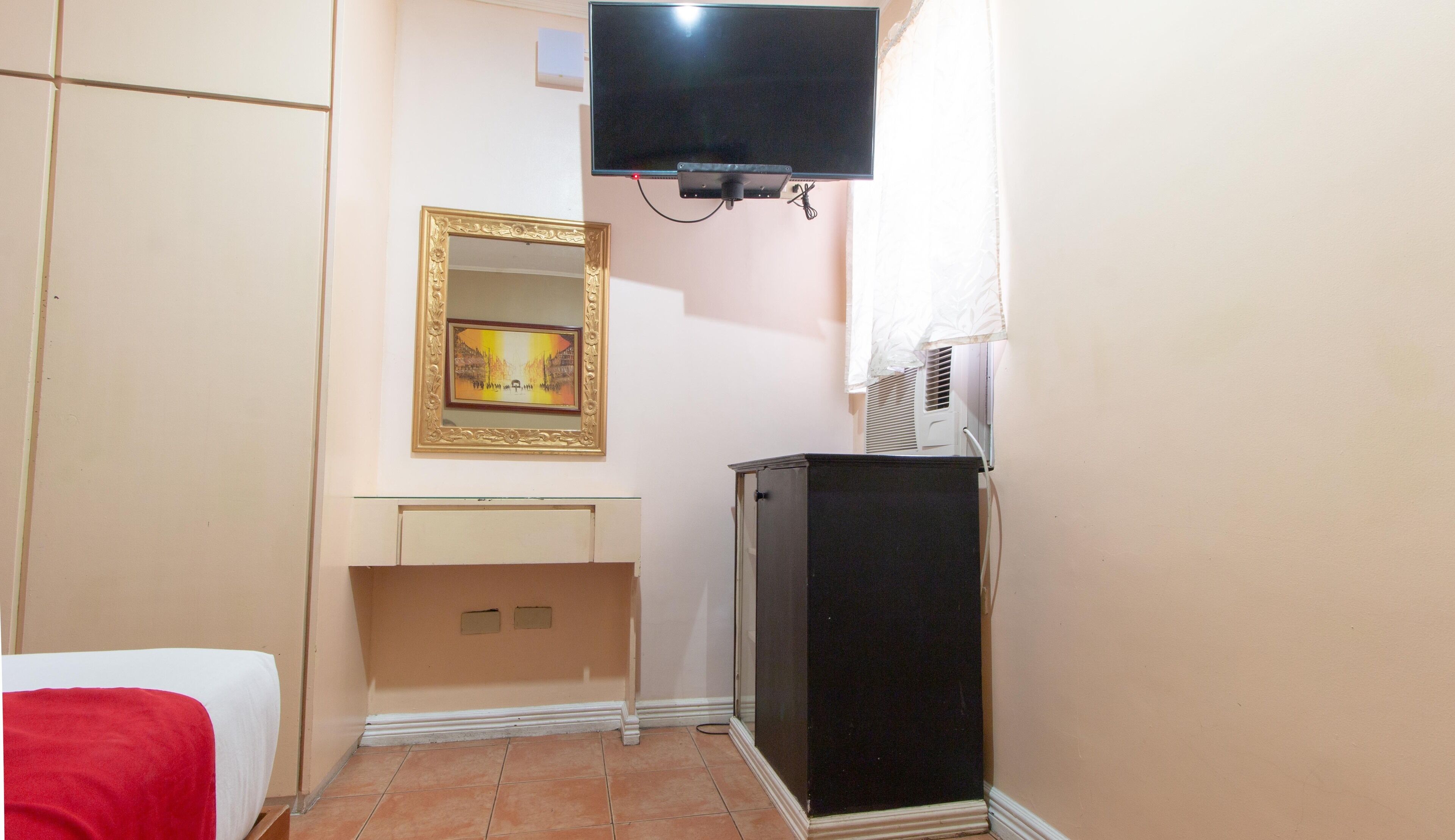 A small room with a bed, a television mounted on the wall, a mirror, and a cabinet.