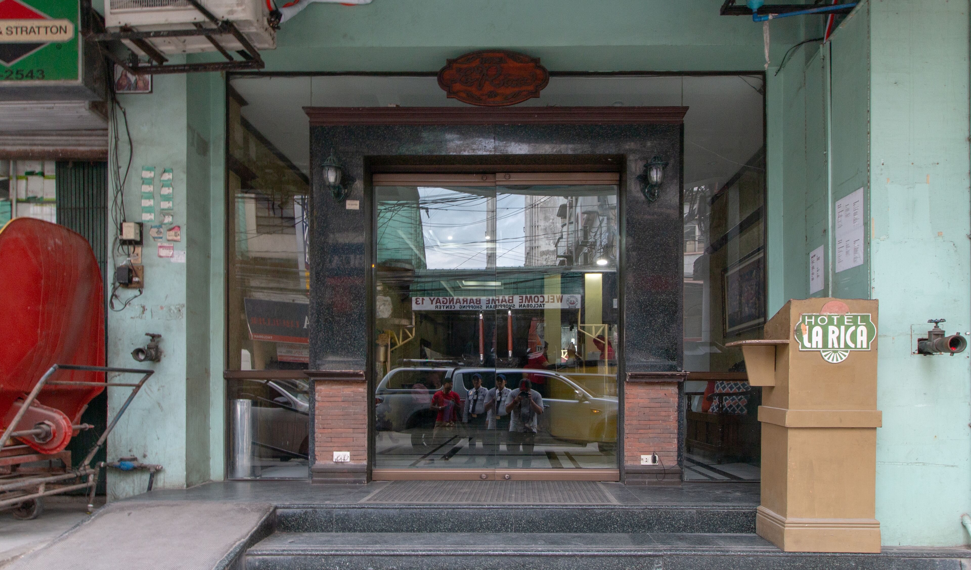 The entrance to a hotel with a glass facade, a signboard above the entrance, and a small podium with a sign.