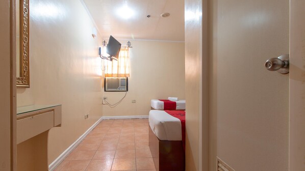 Un pasillo estrecho con una cama y un espejo a la izquierda, un aire acondicionado de pared y una puerta con cerradura a la derecha.