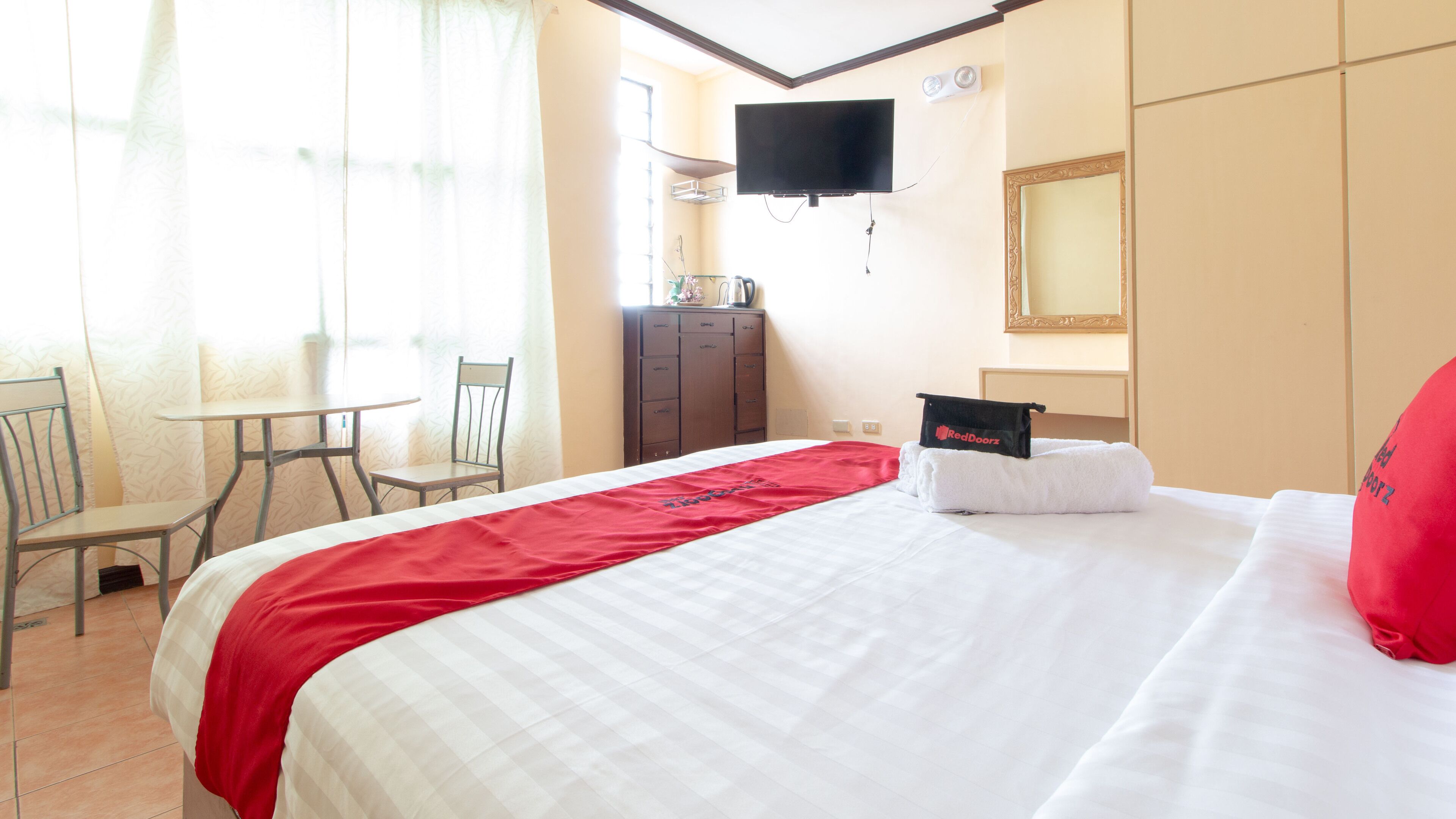 Habitación de hotel con cama, televisor montado en la pared, escritorio con silla y armario.