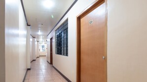 A long, narrow hallway with tiled flooring, wooden doors, and a window with metal bars. - RedDoorz @ Downtown Tacloban (Tacloban)