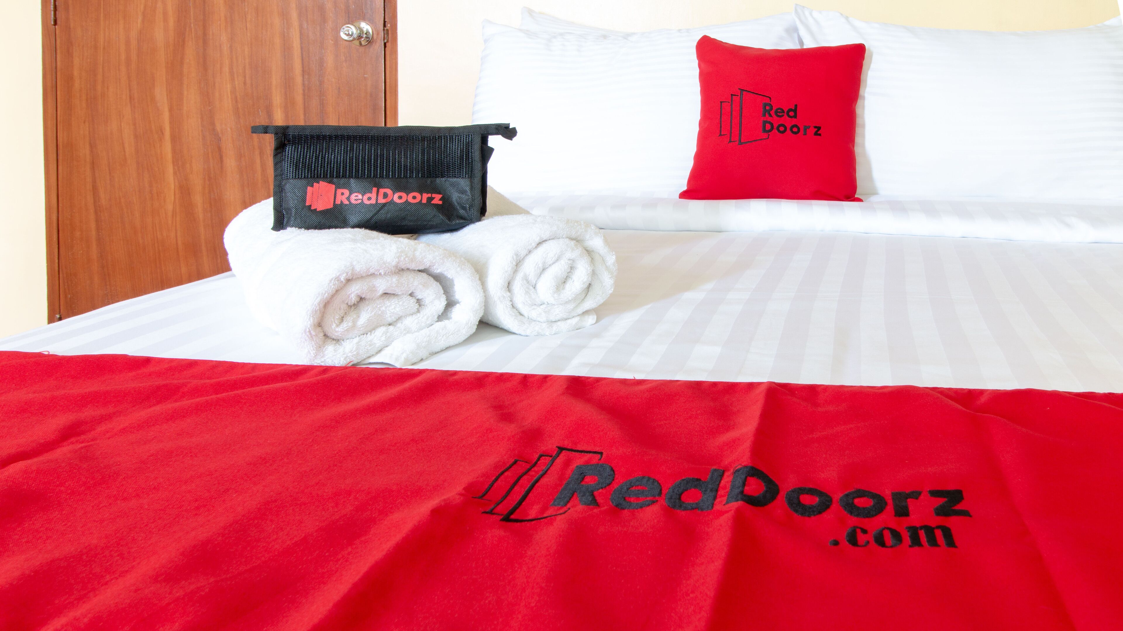 A hotel room with a neatly made bed, a red and black RedDoorz branded pillow, and a matching pillowcase.