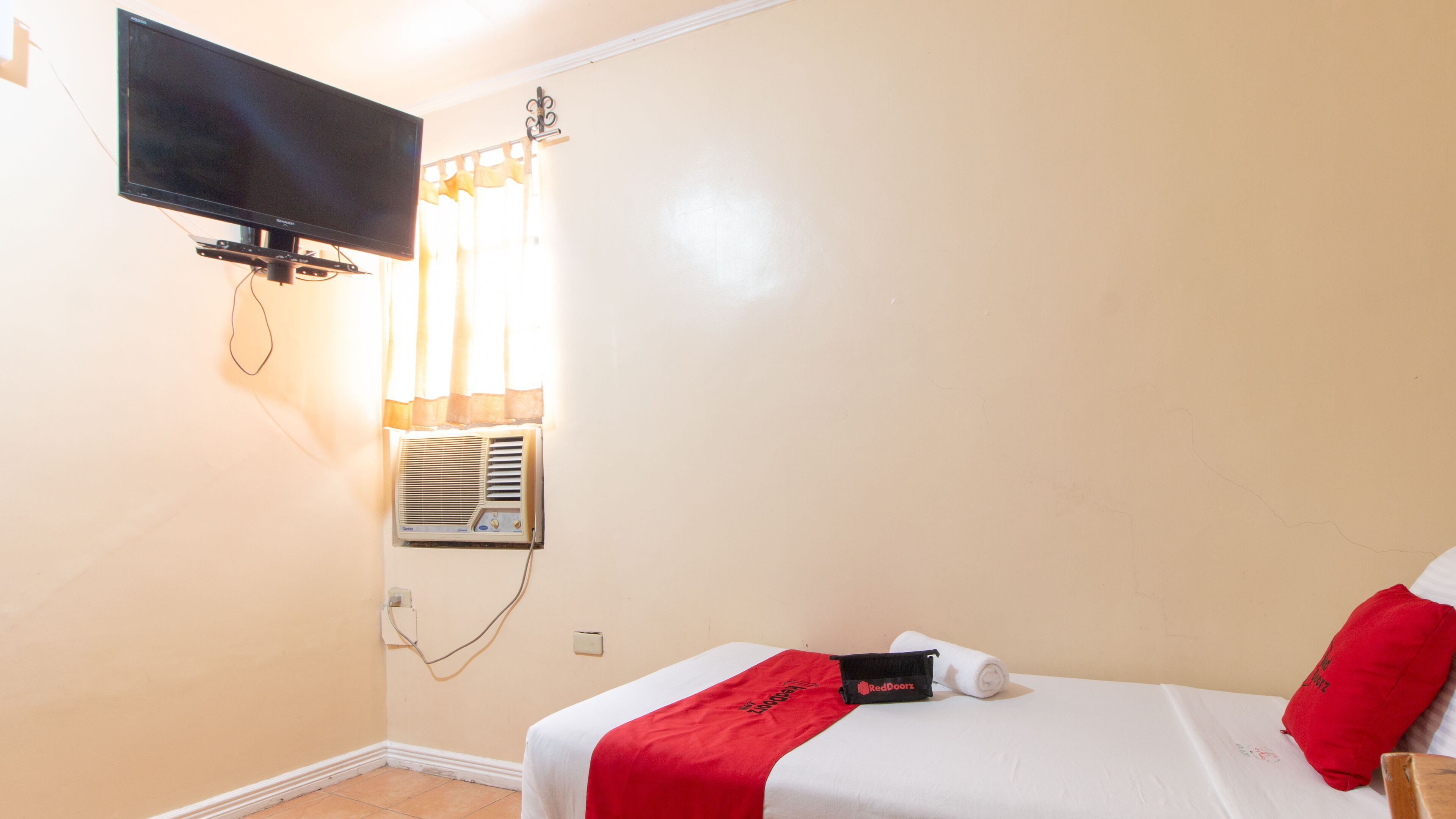 Ein Hotelzimmer mit Bett, Wandfernseher, Klimaanlage und einem fenster mit Vorhängen.