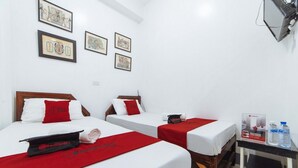 Hotelkamer met twee bedden, elk met een rode sprei en witte lakens. Er hangen prestaties aan de muur, een klein tafeltje met waterflesjes, en een aan de muur bevestigde televisie.