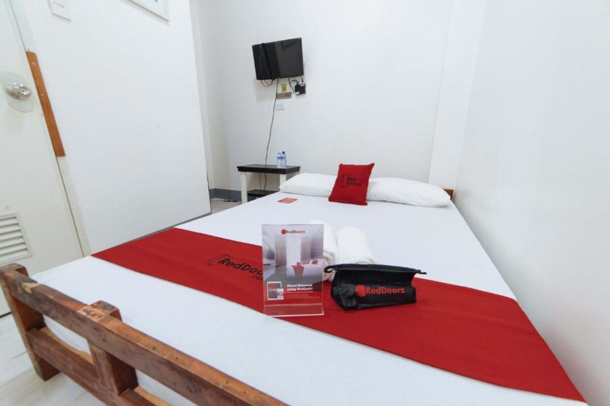 Une chambre d’hôtel avec un lit, une table de chevet, un téléviseur fixé au mur et un sac RedDoorz posé sur le lit.