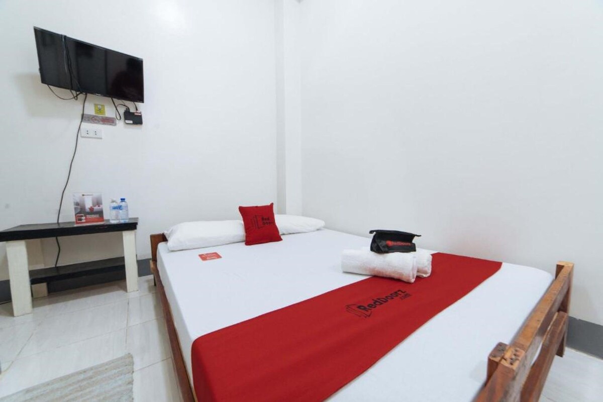 Una habitación de hotel con una cama, un escritorio, un televisor montado en la pared y una manta roja con el logotipo del hotel.