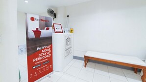 Een receptiegedeelte met een RedDoorz bord, een houten bank en een ventilator aan de muur.