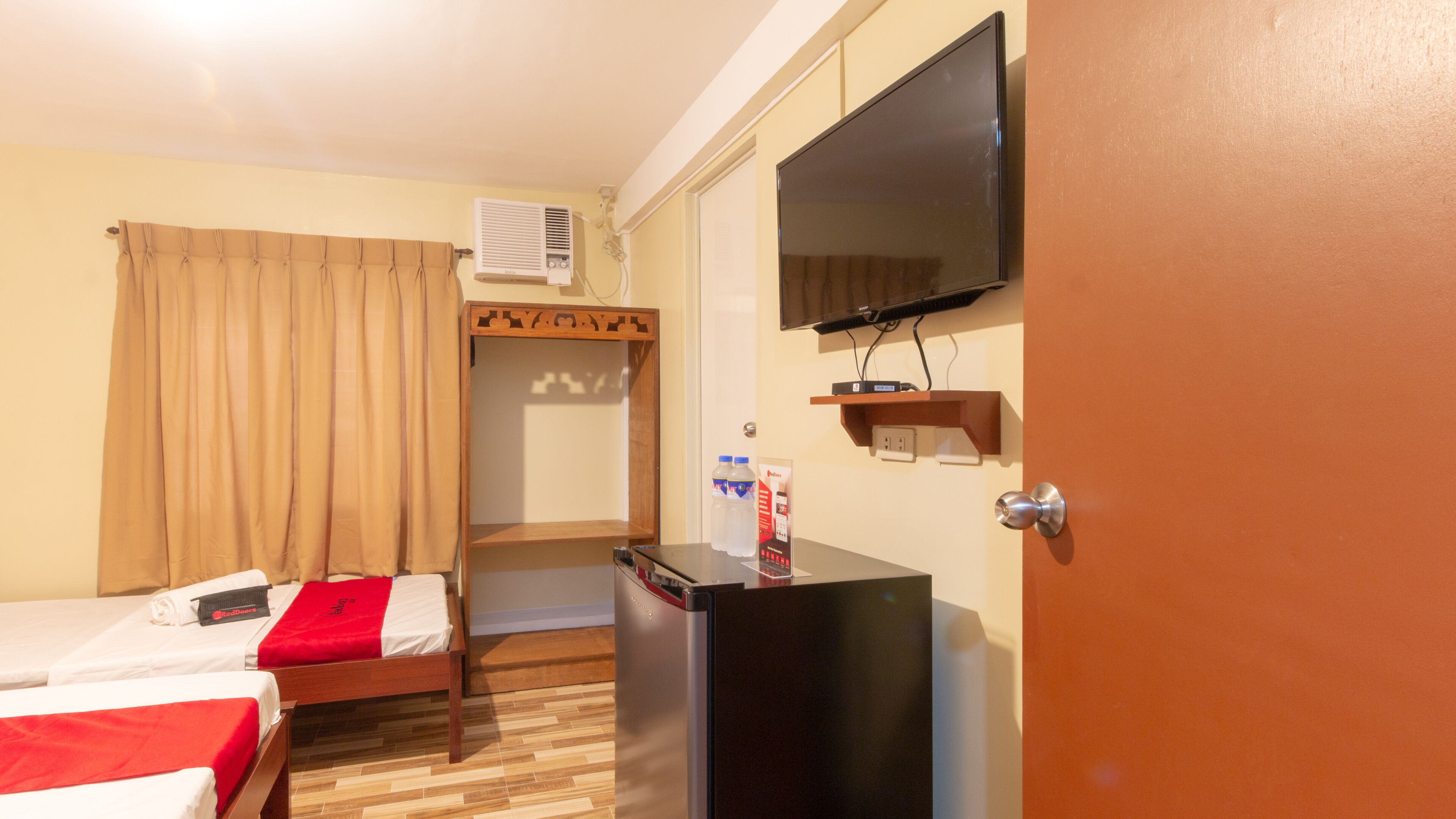 Ein Hotelzimmer mit zwei Betten, einem Fernseher, einem Kühlschrank und einer Minibar.