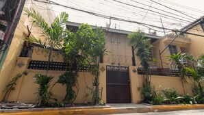 A building with a gated entrance, surrounded by various plants and a yellow curb. - RedDoorz near PNR Espana Station (Manila)