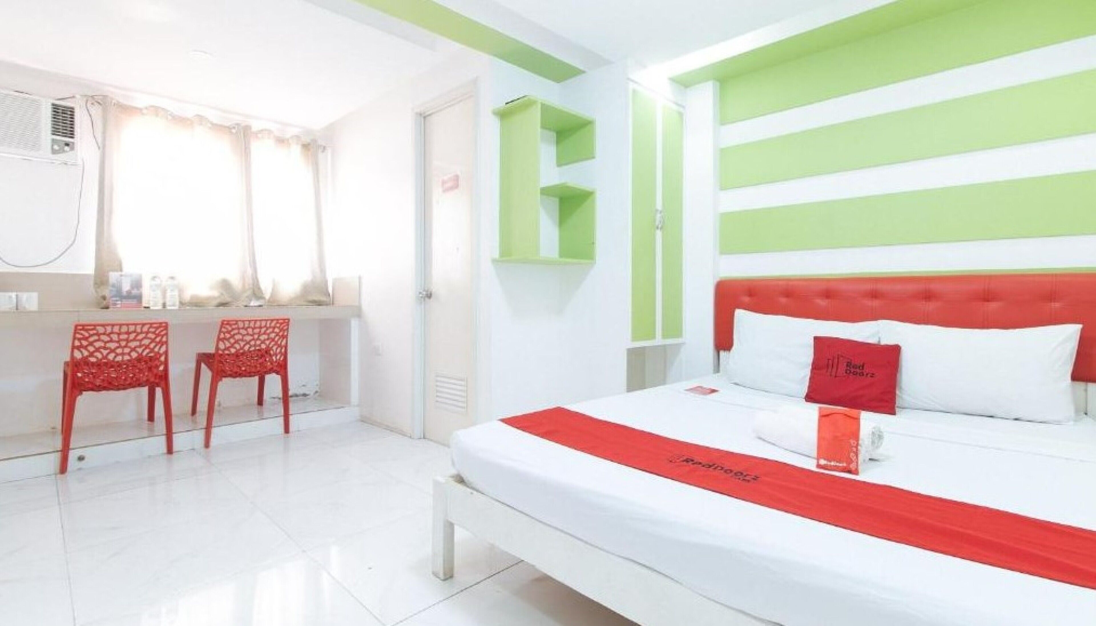 Habitació d'hotel amb llit, escriptori i cadires, i una paret decorativa de color verd.
