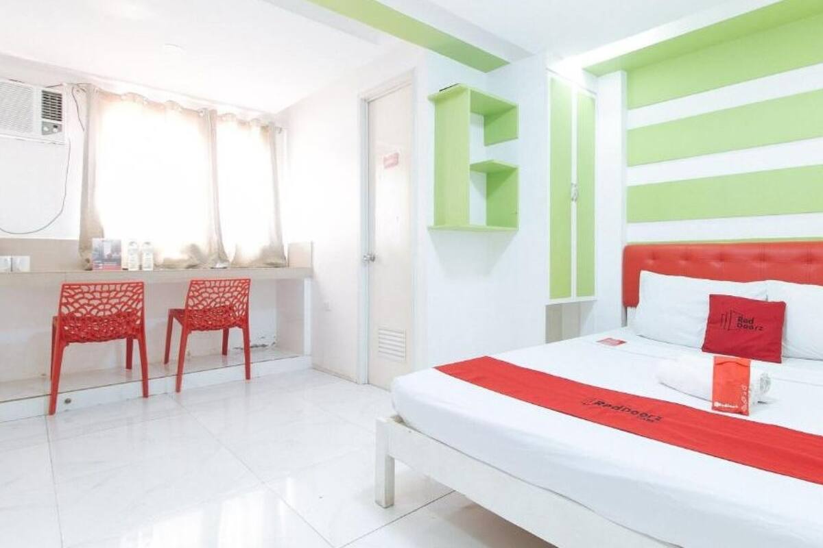 A hotel room with a bed, a desk with chairs, and a green accent wall.