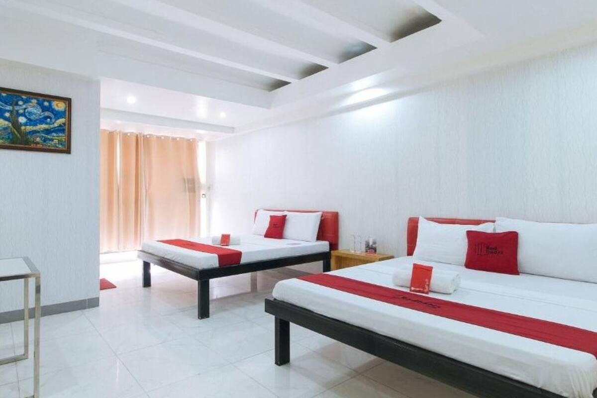 A hotel room with two beds, a table, and a painting on the wall.