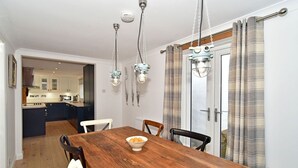 Un comedor con una mesa de madera, sillas y un cuenco de fruta. Arrastran lámparas colgantes sobre la mesa.