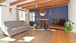 Una sala de estar acogedora con un sofá, un televisor, una chimenea y vigas de madera en el techo.