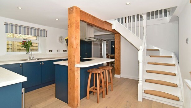Una cocina moderna con una isla central, vigas de madera y una escalera blanca.