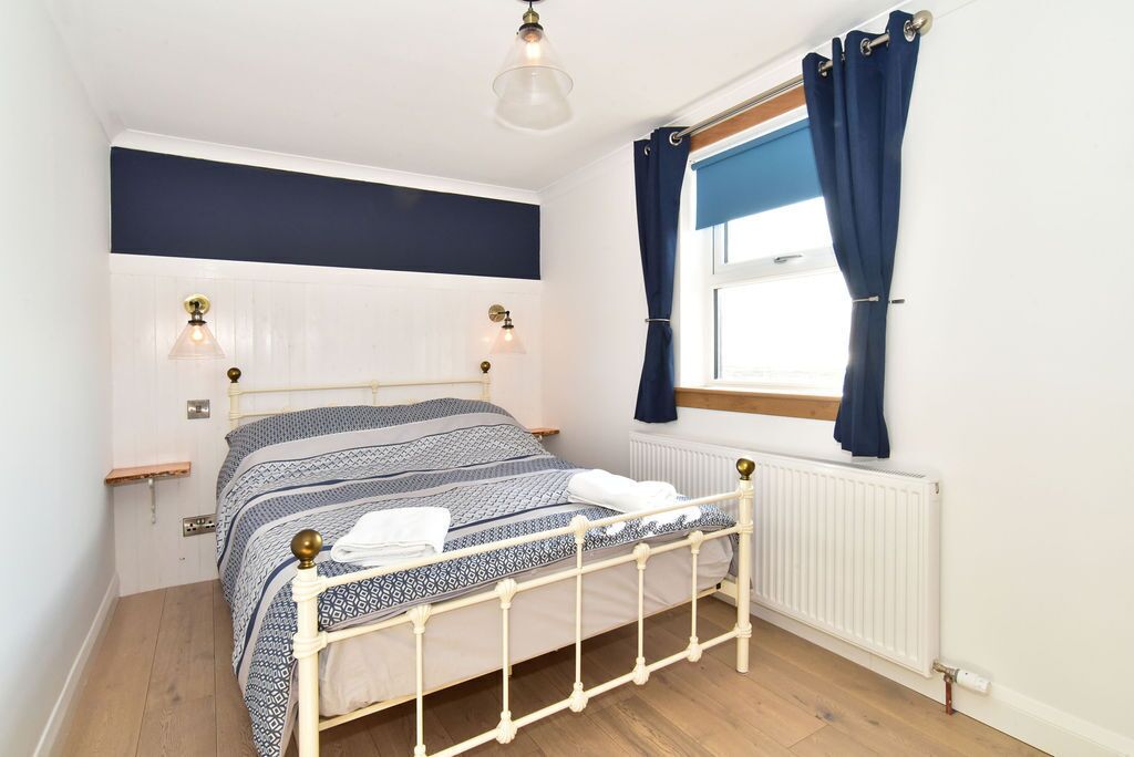 A neatly arranged bedroom with a bed, bedside lamps, a window with curtains, and a radiator.
