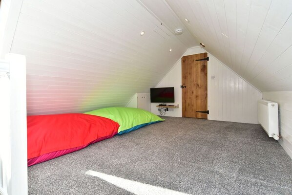 A small attic bedroom with a sloped ceiling, a wooden door, a television, and a colorful bed.