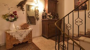 Un escalier orné de rampes en métal ouvragé, un meuble en bois agrémenté d’objets décoratifs, un miroir et un arrangement floral posé sur une table.