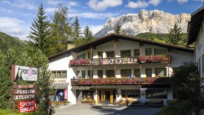 Un hôtel situé au pied d’une montagne, doté de balcons ornés de jardinières et de panneaux indiquant les services sportifs et les prestations proposées.