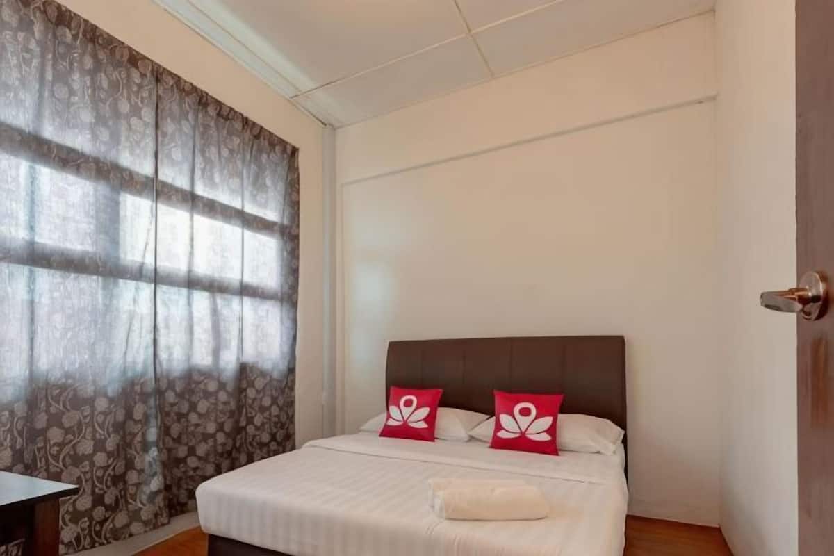 A bedroom with a bed, two pillows, a bedside table, and a window with curtains.