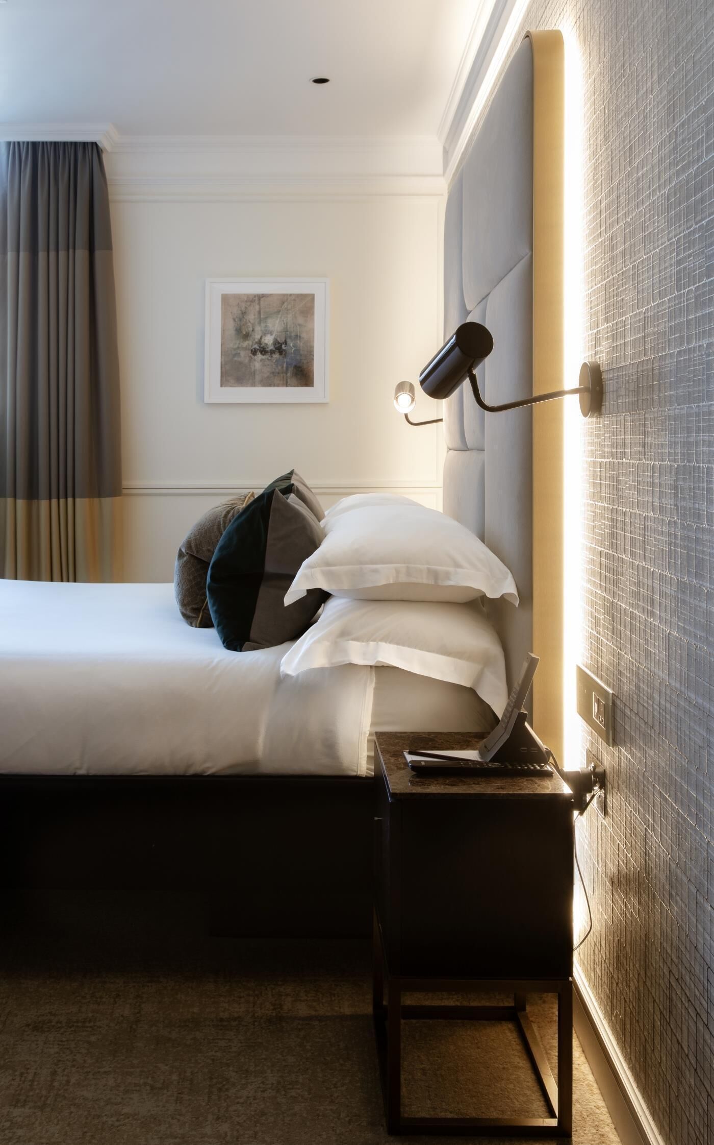A hotel room with a bed, a desk with a laptop, a lamp, and a picture on the wall.