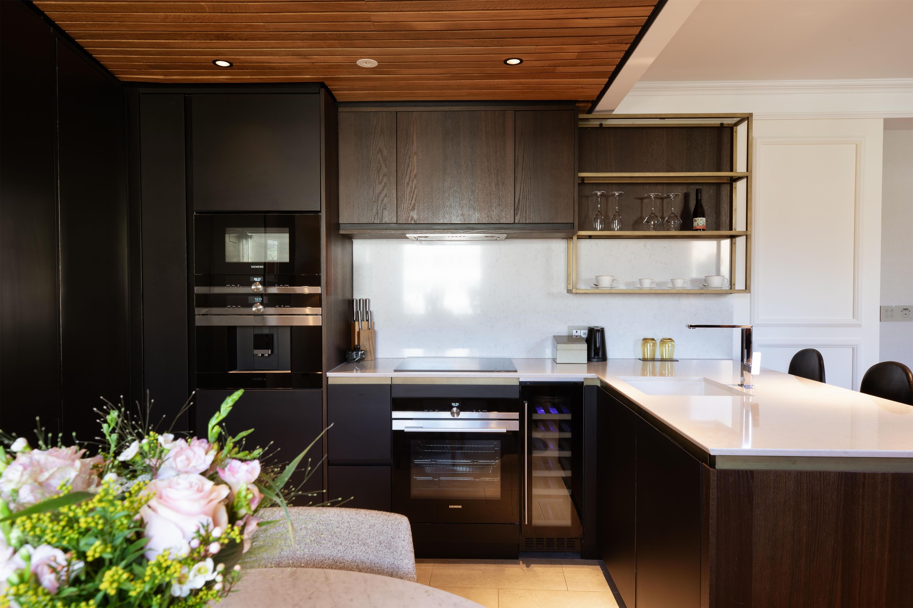 A modern kitchen with built-in appliances, a wooden ceiling, and a dining area with a white table and chairs.