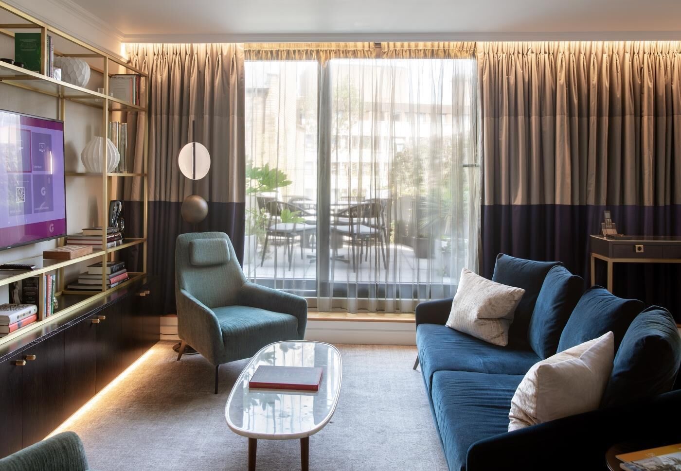 A modern living room with a sofa, armchair, coffee table, and a TV on a shelf.