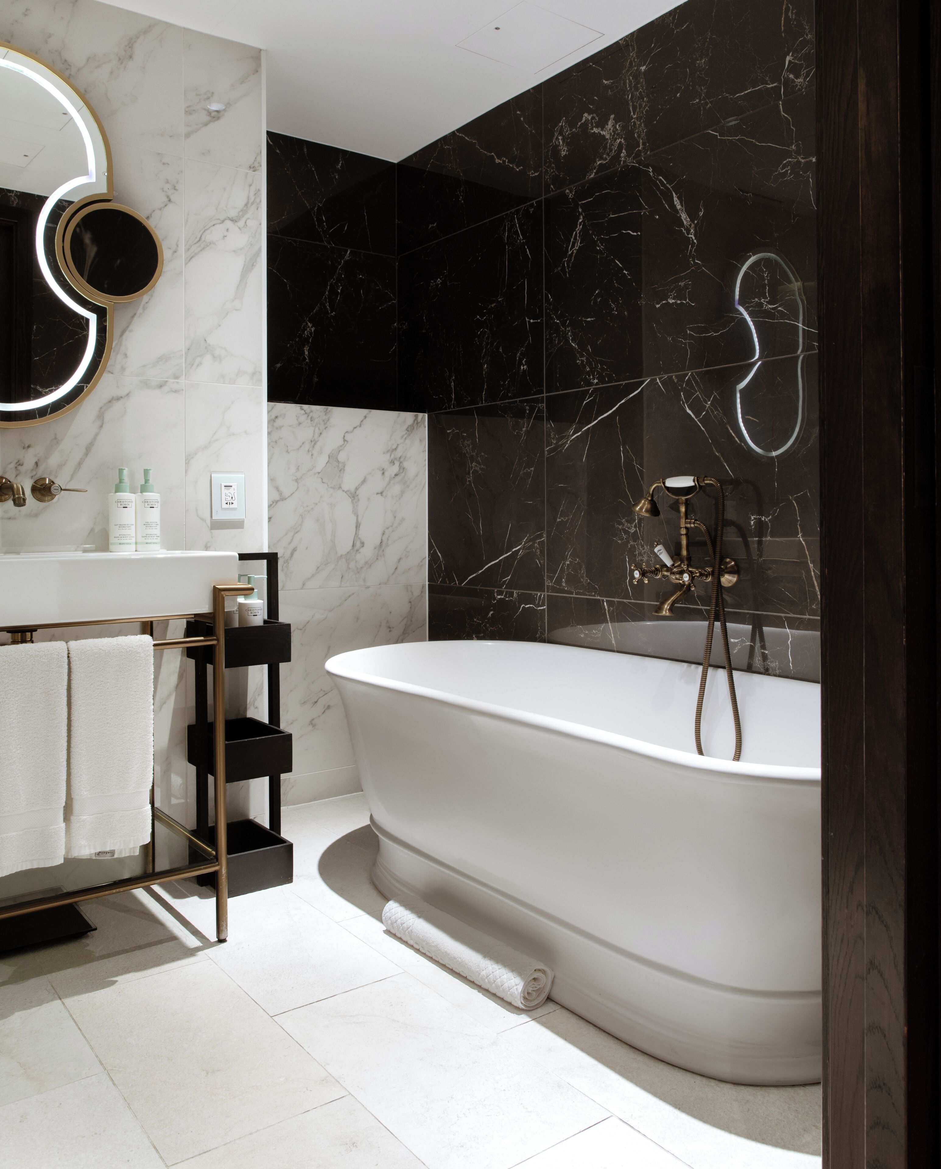 A modern bathroom with a freestanding bathtub, a vanity with a mirror, and marble walls.