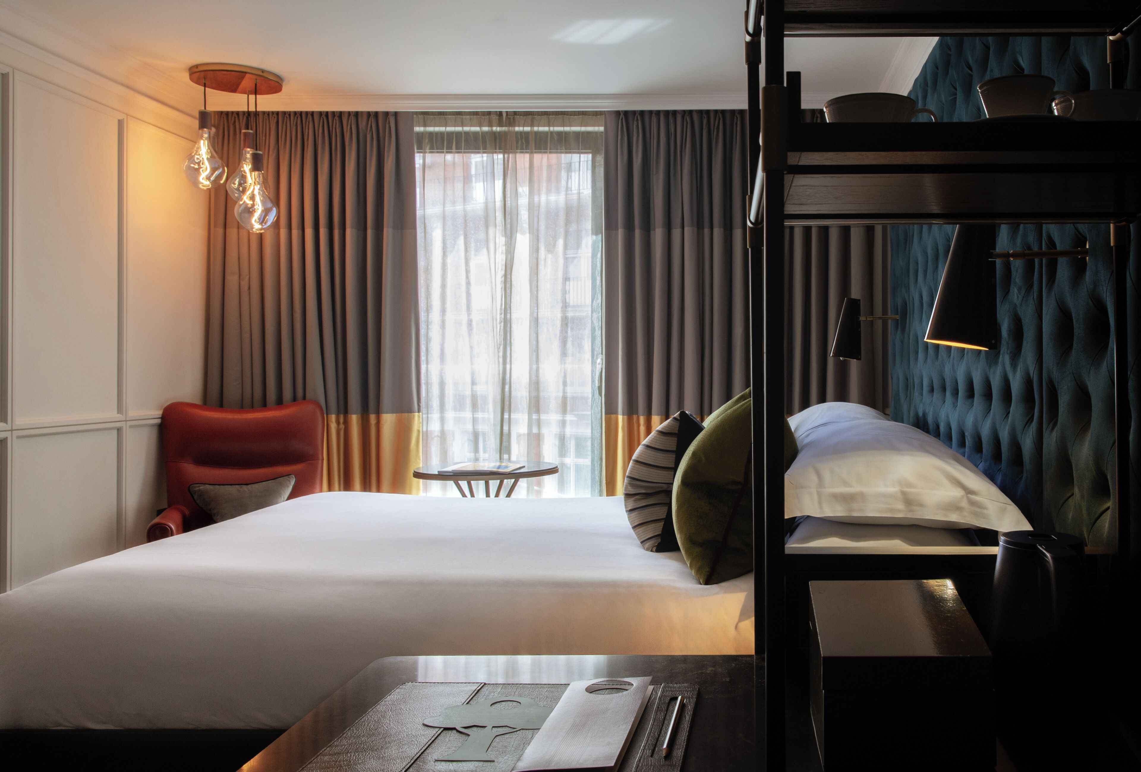 A hotel room with a bed, a red armchair, a small table with a book, and a bunk bed.