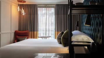 A hotel room with a bed, a red armchair, a small table with a book, and a bunk bed.