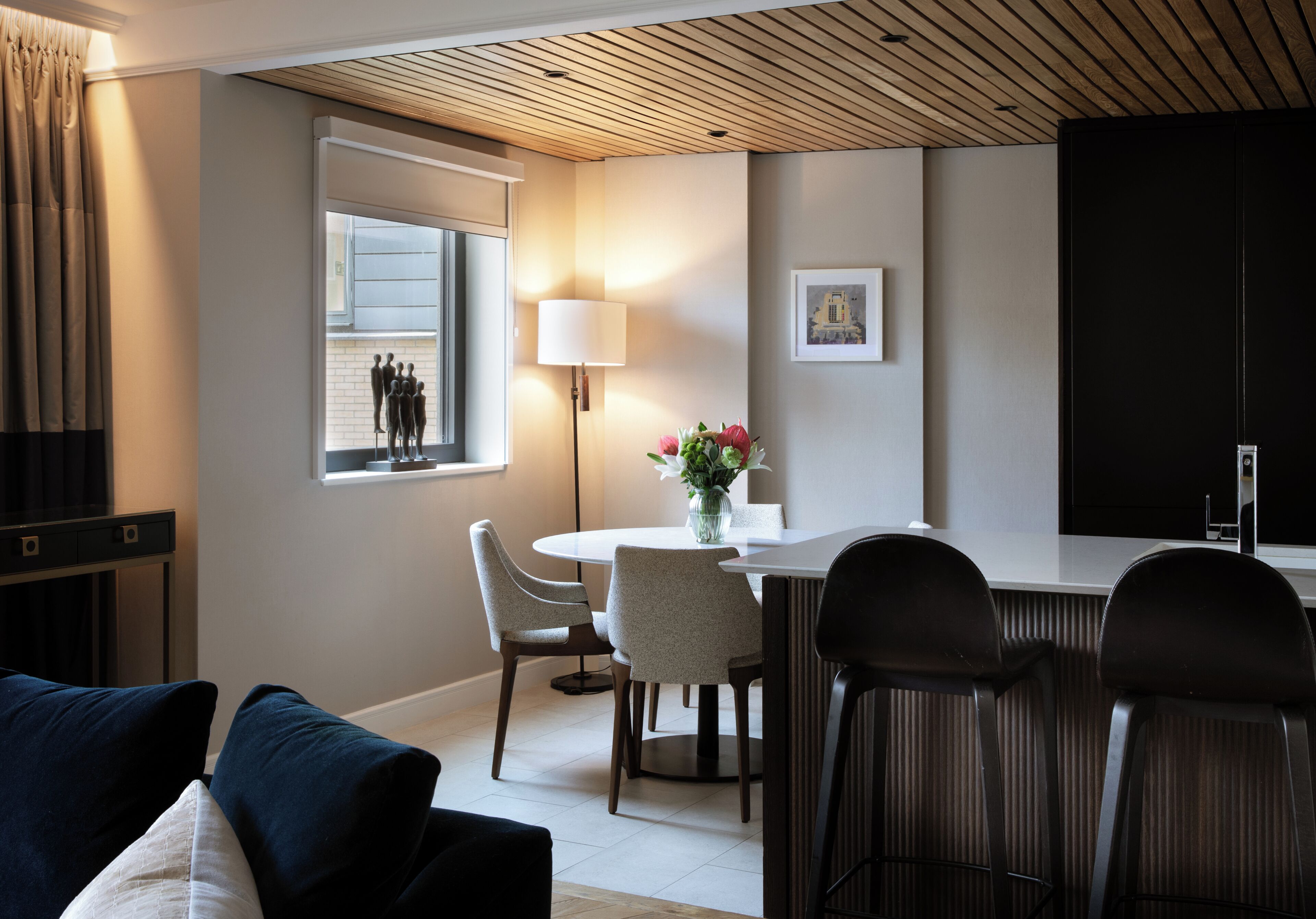 A modern dining area with a round table, two chairs, a lamp, and a window with curtains.