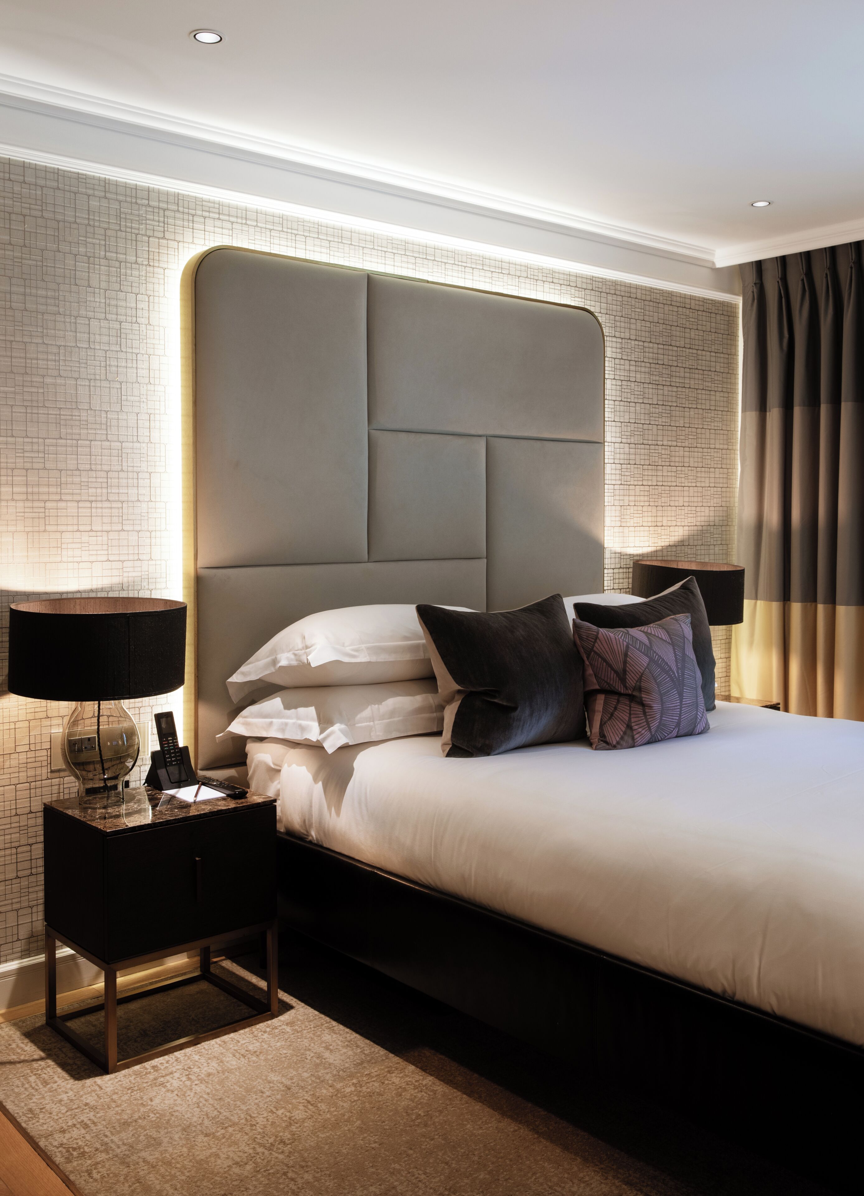 A hotel room with a large bed, a nightstand with a lamp, and a modern headboard.