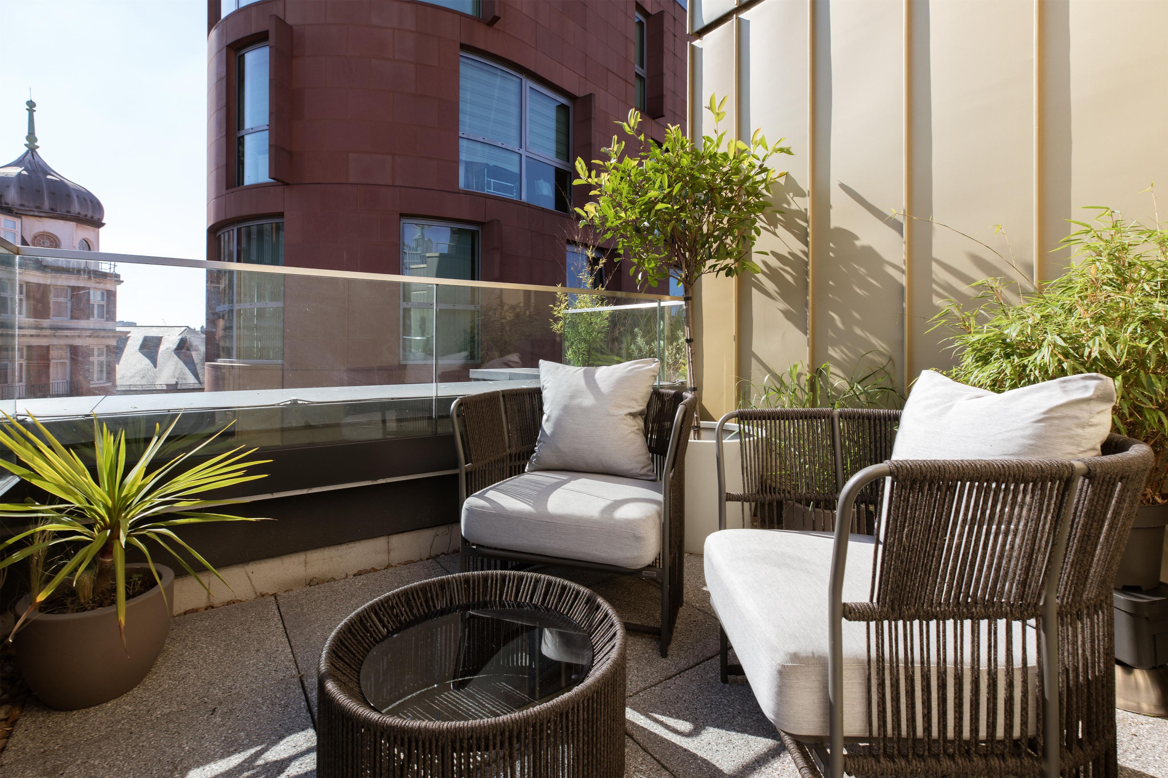 A balcony with wicker furniture, a potted plant, and a view of a building with a dome.